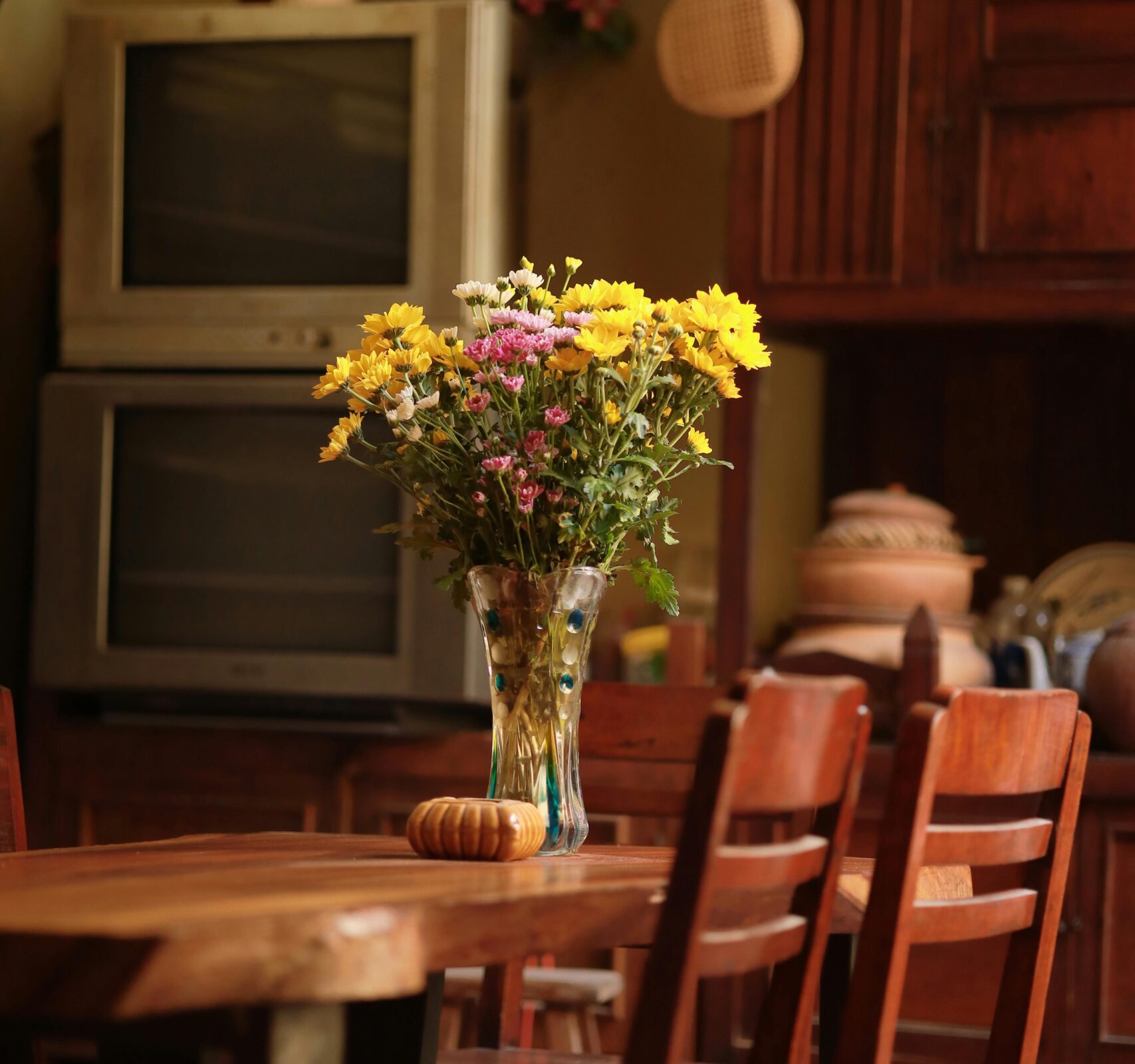 Rustic kitchen featuring vintage decor, wooden table, and flowers in a vase.
